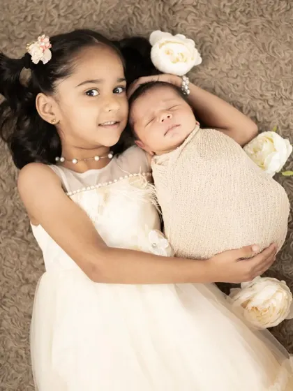 A beautiful overhead shot of a big sister holding her new baby sibling. We use soft, neutral tones to create a dreamy and angelic feel for our newborn and sibling sessions.