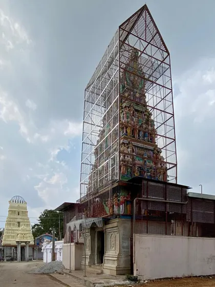A wider view of the temple enclosure, showing the contrast between the intricate, colorful gopuram and the stark, geometric form of its protective cage.