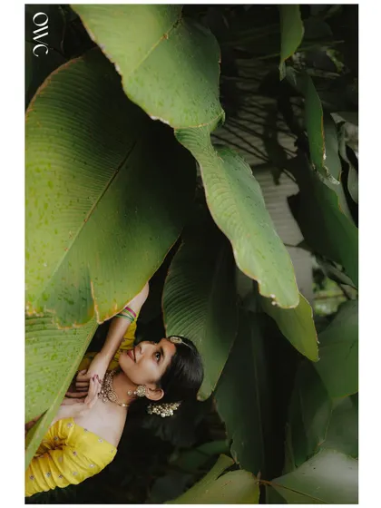 An artistic shot of the bride looking up from beneath large green leaves, creating a unique and natural frame.