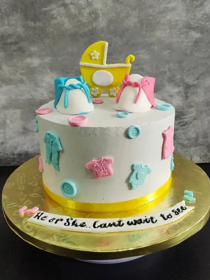 "He or She, Can't wait to see." This baby shower cake is decorated with tiny fondant baby clothes, shoes, and buttons in pink and blue.