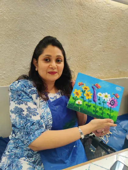 An adult guest at Nishka's birthday party proudly shows the colorful floral canvas she painted alongside the children.