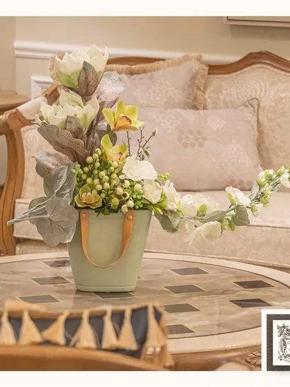 In the symphony of colors, my artificial flower arrangements dance with grace. This arrangement, in a unique pale green bucket-style vase, creates a melody of perpetual bloom on a coffee table.