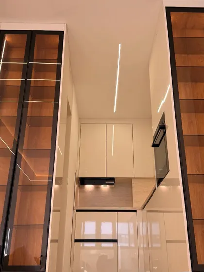 A different angle of the stunning white kitchen from our featured section, emphasizing the ceiling height and the verticality of the tall display units with integrated lighting.