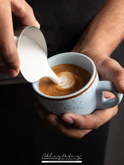 This shot captures the craft of a barista, focusing on the hands as they create latte art. It adds a human element and tells a story of skill and passion behind the coffee.