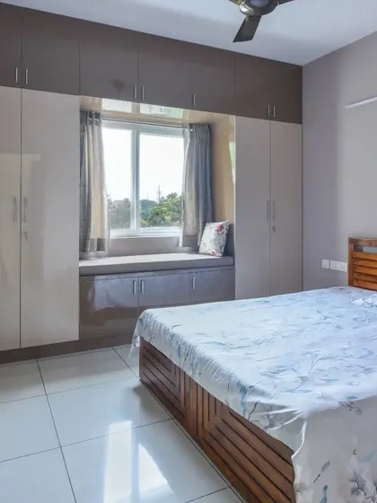 This bedroom features a practical and stylish wardrobe with a built-in bay window seating area. The glossy, dual-tone finish of the wardrobe adds a modern touch.