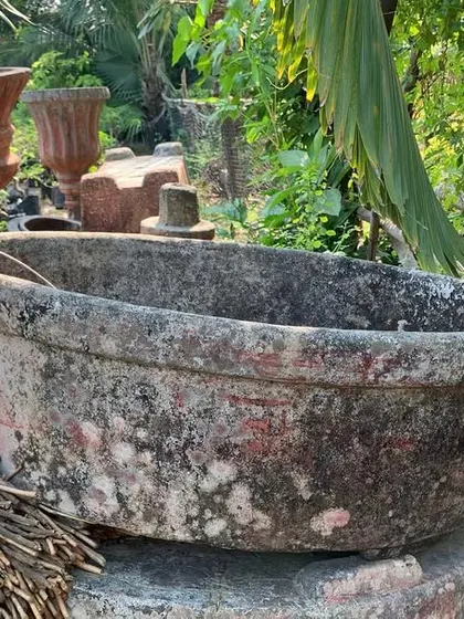 A large, rustic stone basin waiting to be installed as part of a water feature or a unique, large-scale planter.