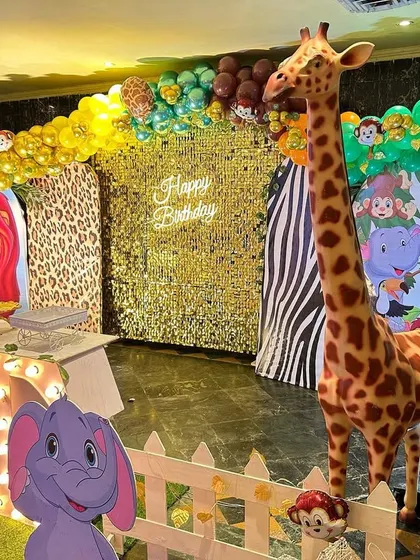 A detailed jungle-themed first birthday stage. The setup includes leopard and zebra print backdrops, a gold shimmer wall, and large "ONE" marquee letters.