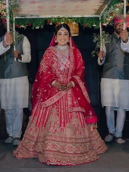 The bride's grand entrance under the phoolon ki chadar. Her radiant smile and stunning red lehenga make for an unforgettable bridal moment.
