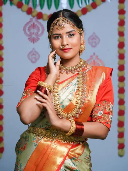 A vibrant South Indian bridal look. The bright colors of the saree and the elaborate temple jewelry are the focus of this celebratory portrait.