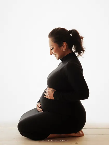 A kneeling profile pose in a simple black turtleneck dress against a white background creates a chic, minimalist, and modern maternity portrait.