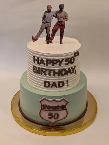 A special two-tier cake for a dad's 50th birthday. The design features a "Route 50" sign and a personalized topper showing a picture of him with his son.
