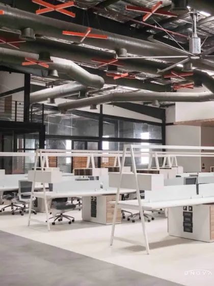 An aerial view of the open-plan workstation area at the DesignCo industrial office. The design utilizes the building's height and industrial character, with exposed MEP and large fans for air circulation.