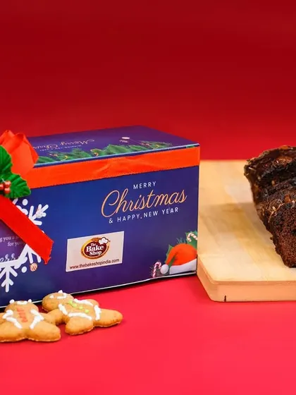 A beautifully styled shot of our Christmas gift tin, accompanied by slices of rich plum cake and gingerbread cookies. This showcases our elegant packaging and classic holiday treats.