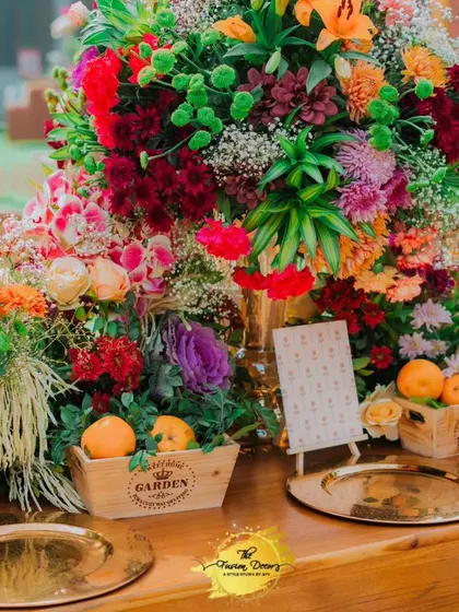A feast of colours and textures on this tabletop, with overflowing floral arrangements, fresh oranges in wooden crates, and gleaming gold plates.