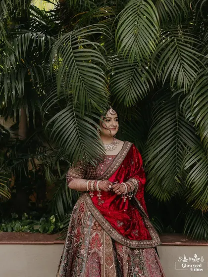 A portrait of the bride, Drashti, in her rich velvet lehenga, posing against a backdrop of tropical leaves.
