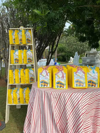 A fun display of party favors for a "Wheels on the Bus" themed event. The yellow goodie bags are neatly arranged on a ladder shelf, ready for the little guests to take home.