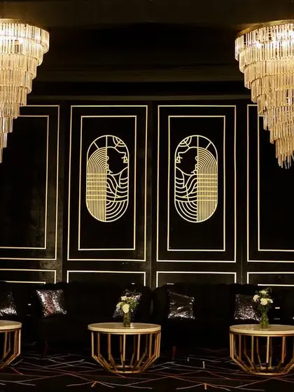 A moody and luxurious Sangeet lounge with a black and gold Art Deco theme, featuring plush seating and magnificent tiered chandeliers.