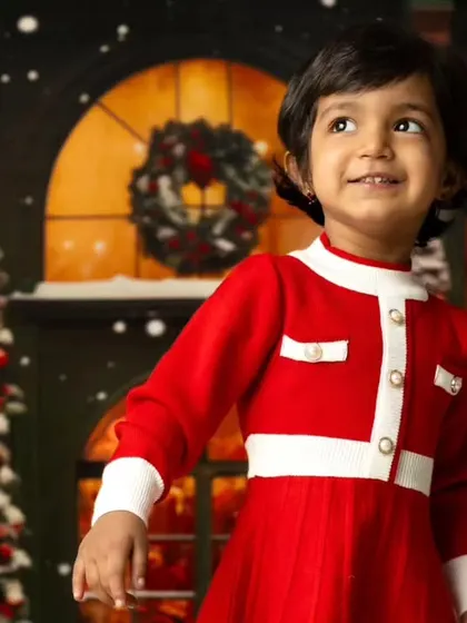 A little girl dressed in a classic red Christmas dress, looking up with wonder at the holiday lights.