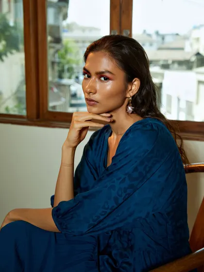 A beautiful indoor portrait using natural window light. The deep blue of the dress and the warm wooden tones of the chair create a rich and elegant color palette.