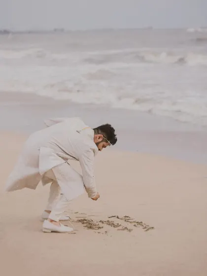A candid moment of the groom writing in the sand on a Goa beach. These little, personal moments add a unique touch to your destination wedding story.