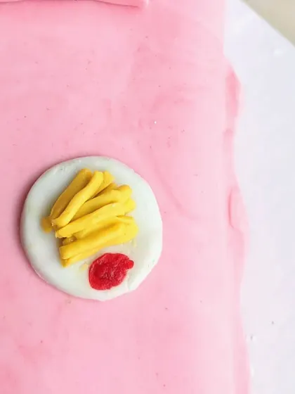 A miniature plate of french fries with a side of ketchup, all made from fondant. These tiny food toppers are perfect for a foodie-themed cake.