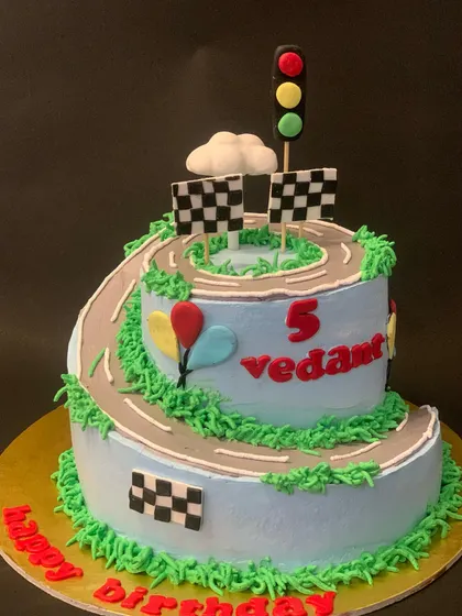 A fun two-tier race track cake for a 5th birthday. I created a winding road that spirals up the cake, complete with checkered flags and a traffic light.