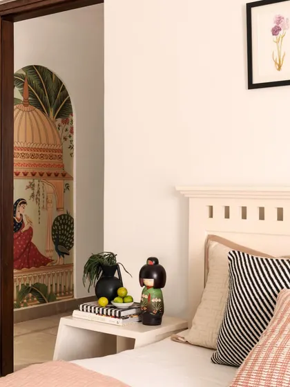 In the guest bedroom, a peek of a traditional Indian mural is visible through the doorway, adding an element of surprise and cultural context. The bedside styling is kept simple to let the artwork shine.