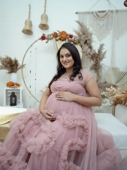 A lovely, direct-to-camera portrait in the boho setting. The mother-to-be is seated comfortably, with the elaborate pink gown creating a beautiful frame around her.