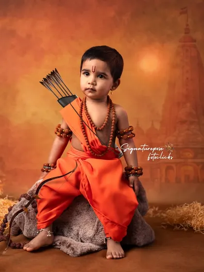 This portrait of a young boy as Rama captures a regal and composed look. The detailed costume, complete with a quiver of arrows, and the temple backdrop create a complete and immersive visual story.