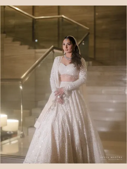 A vision in white. This full-length portrait on the staircase showcases the bride's stunning white lehenga and her poised, elegant presence.