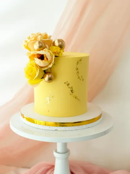 A minimalist yellow cake with gold leaf accents. The simple design is elevated by a beautiful arrangement of yellow silk flowers and gold spheres.