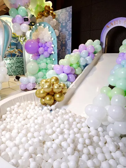 A white ball pit with a slide, decorated with pastel and gold balloons, providing endless fun for the little guests at the carnival party.