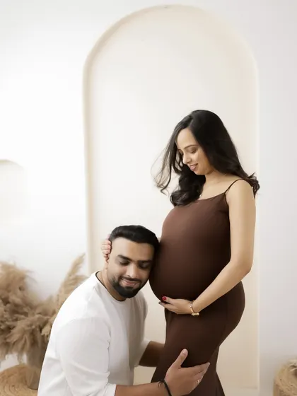 A simple, beautiful moment of connection. The dad-to-be rests his ear against the baby bump, sharing a quiet moment with his partner and their little one.