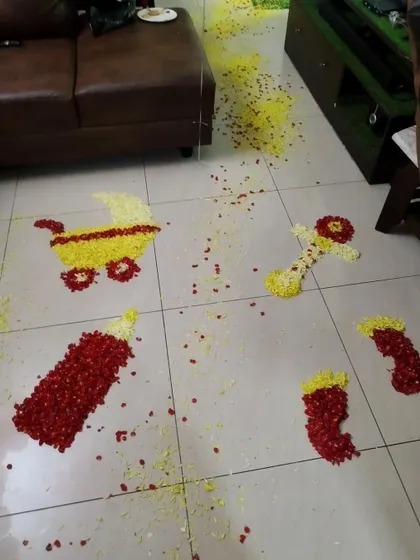 Creative floor decorations made from flower petals, shaped into a baby carriage, bottle, and booties, to welcome a new baby home.