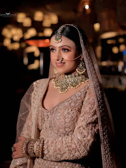 A three-quarter portrait of the bride looking away with a gentle smile. The soft lighting enhances the delicate embroidery on her pastel lehenga and the sparkle of her jewellery.