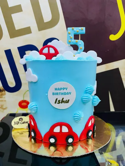 A tall 3kg cake for a 5th birthday, decorated with red toy cars and fluffy buttercream clouds.