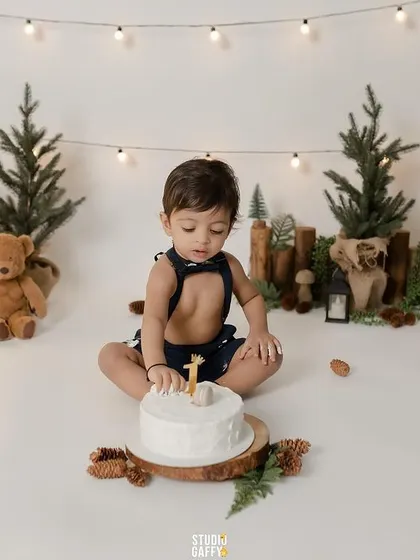 A portrait of the birthday boy with his cake before the fun begins, surrounded by teddy bears and pine trees.