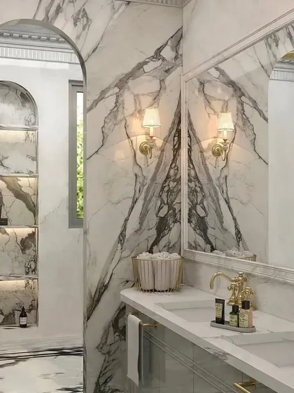 Marble's dramatic veining instantly invites opulence into a space. Here, I used book-matched marble slabs to create a stunning, symmetrical feature wall behind the vanity, complemented by classic gold fixtures and sconces.