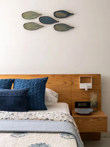 A serene bedroom that embodies simplicity and sophistication. The natural wooden headboard is paired with rich blue pillows and stylized fish wall art, creating a calm, uncluttered ambiance perfect for unwinding.