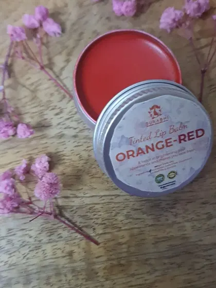 The Orange-Red Tinted Lip Balm is a vibrant, cheerful shade. It brightens your appearance while delivering the same moisturizing benefits as the rest of my lip care line.