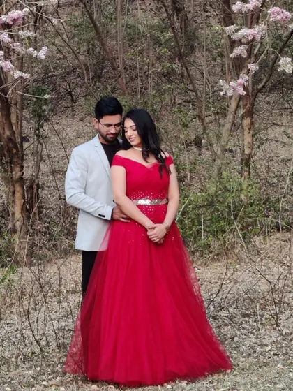 A romantic stroll through a blossoming forest. This off-shoulder red ball gown with a sparkling belt adds a touch of timeless elegance to their pre-wedding photos.