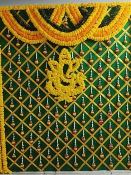 A stunning backdrop for a housewarming pooja, featuring a Ganesha motif made entirely of yellow marigold flowers against a traditional green background.