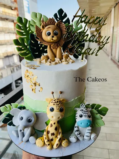 A slightly different angle of the jungle safari cake, highlighting the gold 'Happy Birthday' topper and gold leaf details.