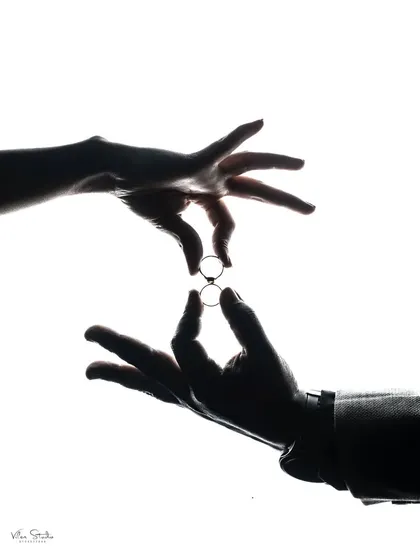 A close-up silhouette shot of the couple's hands exchanging rings. This is a powerful, symbolic image that focuses on the act of commitment.