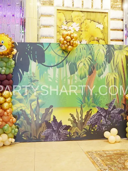 A jungle-themed photo backdrop with a lush forest illustration, flanked by balloon columns in earthy tones and a lion foil balloon.