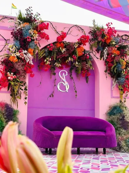 The main stage for a carnival-themed event, featuring a bold purple sofa against a pink backdrop with the couple's monogram.
