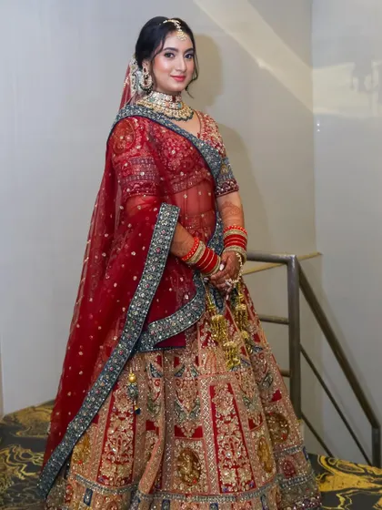 A full-length shot of the bride on a staircase, showcasing her magnificent red and gold lehenga.
