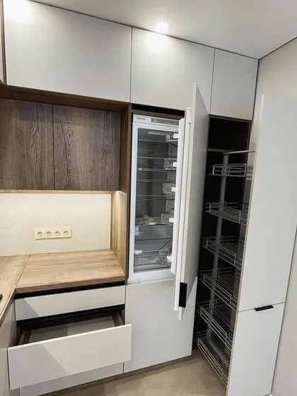 A close-up of the storage solutions in this dual-finish kitchen. It showcases a tall pull-out pantry unit next to an integrated fridge, offering immense and easily accessible storage capacity.