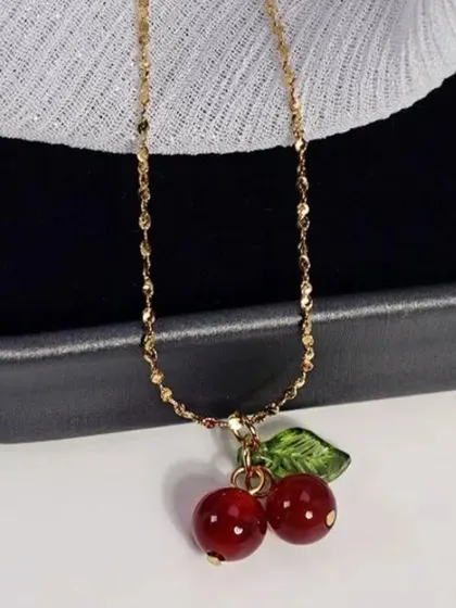 A close-up of the playful cherry charm necklace against a dark background, highlighting the vibrant red beads and delicate gold-toned chain.
