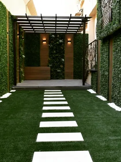 A narrow walkway transformed into a striking entryway. The path is flanked by tall artificial green walls and leads to a raised deck with a pergola, creating a dramatic sense of arrival.